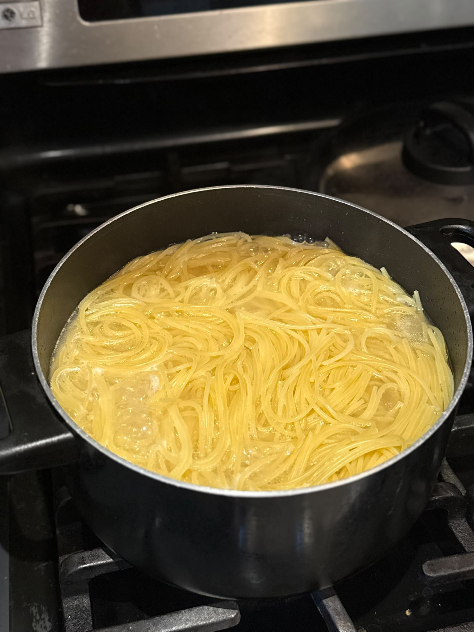 Spaghetti cooking in well-salted water — save a couple of mugs of this starchy water before draining; it's what makes the sauce creamy.